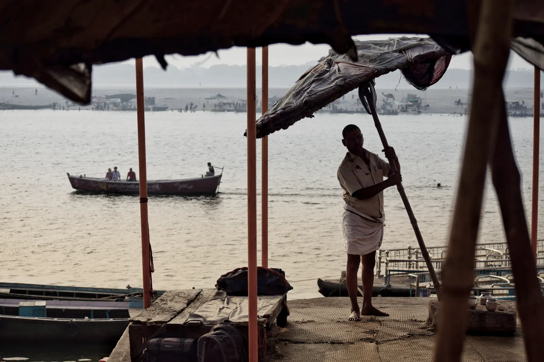 A boatman under a ghat umbrella looking out over the river